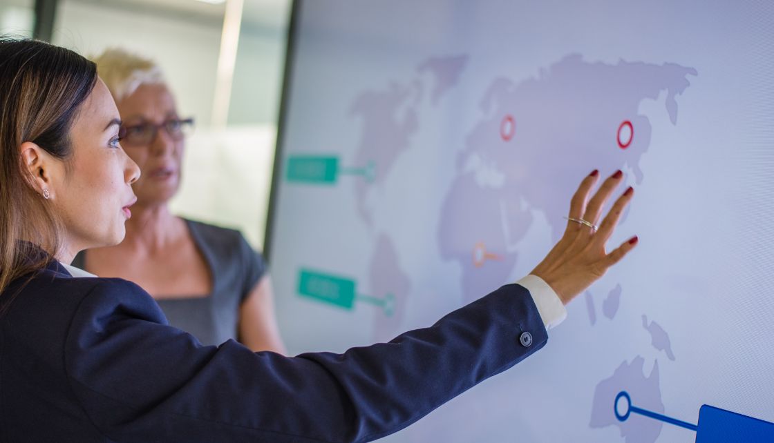 Two women coworkers looking at data points on a world map